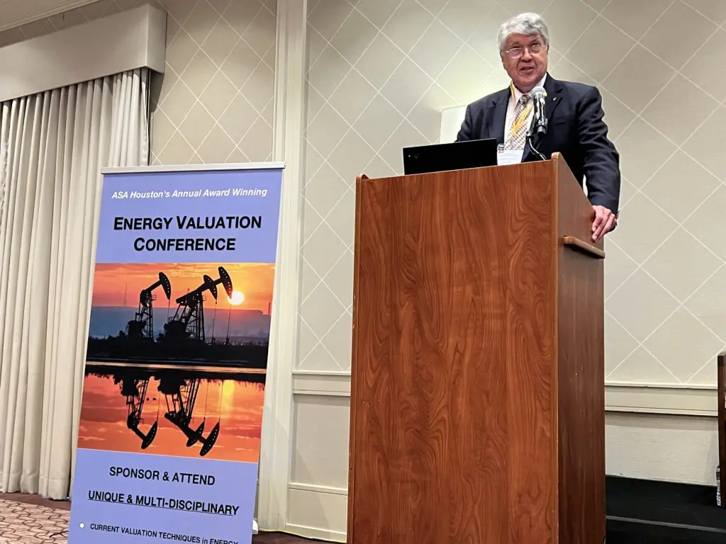 A man standing at the podium in front of an oil well.
